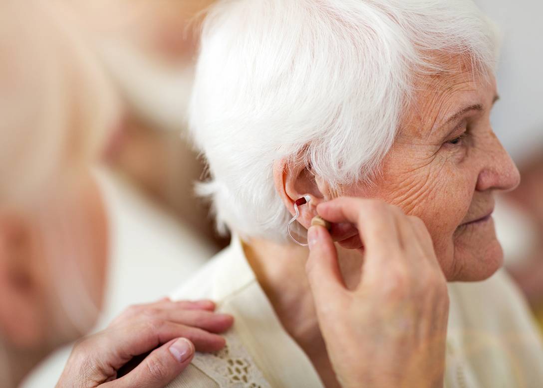 Eine Person setzt einer älteren Frau ein Hörgerät ins Ohr.