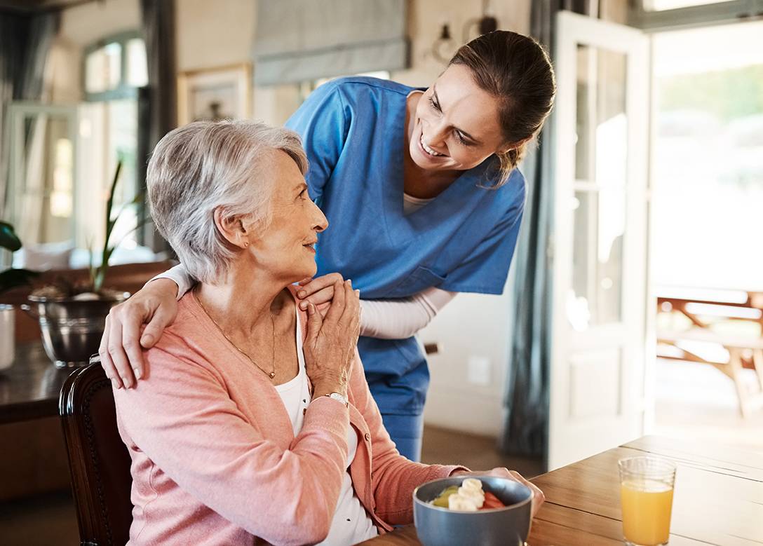 Eine weibliche Pflegekraft beugt sich freundlich über eine ältere Frau