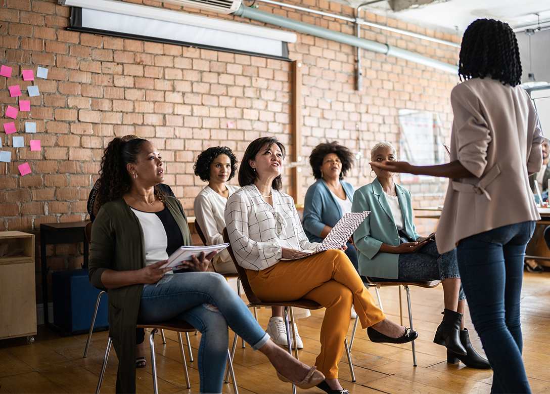 Mehrere Frauen sitzen gemeinsam in einem Seminar, eine weitere Frau steht vor der Gruppe