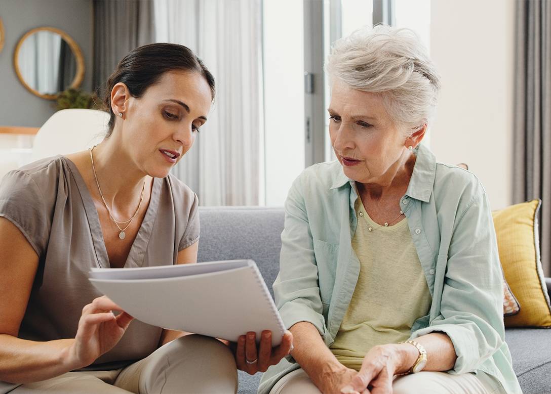 Eine Pflegekraft liest zusammen mit einer älteren Frau ein Dokument