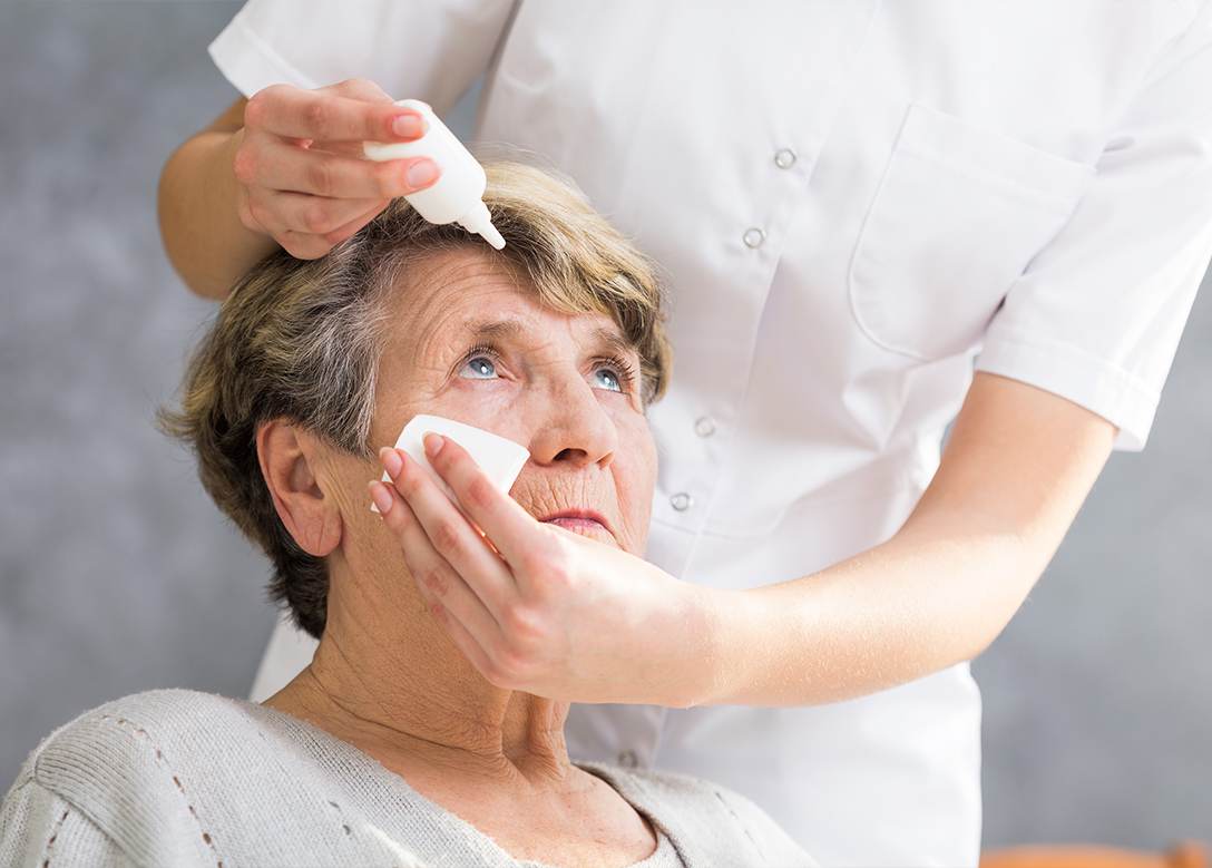 Eine Pflegekraft verabreicht einer älteren Frau Augentropfen.